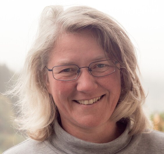 White woman with small glasses and grey/white hair smiles friendly into the camera.
